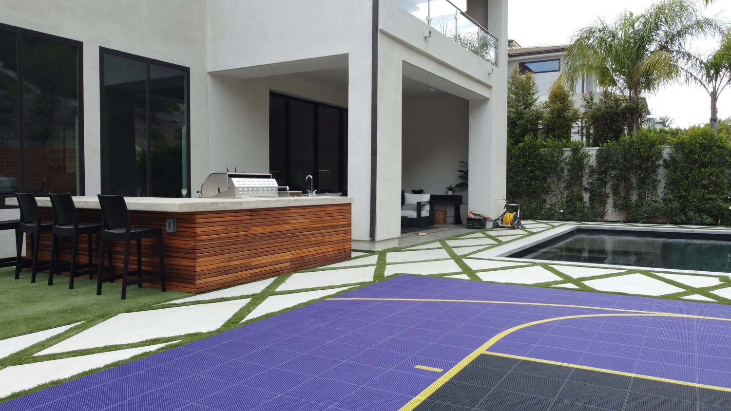 Modern backyard in los angeles designed by smart swim pool construction along with a swimming pool, outdoor seating area, and a built-in barbecue counter, with a basketball court in the foreground.