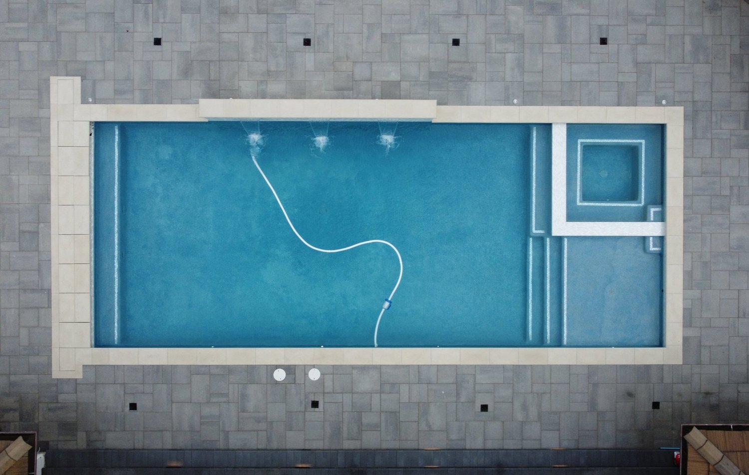 Top-down view of an elegant swimming pool surrounded by grey tile outdoor space designed by smart swim pool construction.